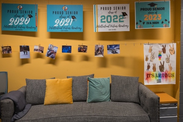 Coach in front of bright yellow wall with college penants hanging across the wall above the couch