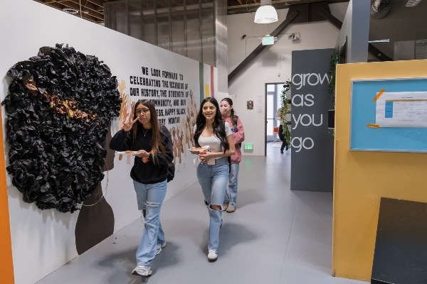 3 IVA students walk down hall with mural on the wall